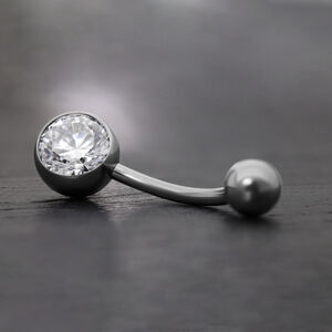 Elegantes Bauchnabelpiercing mit Kristall Schwarzes Bananabell aus Titan mit klarem Kristall auf grauem Hintergrund