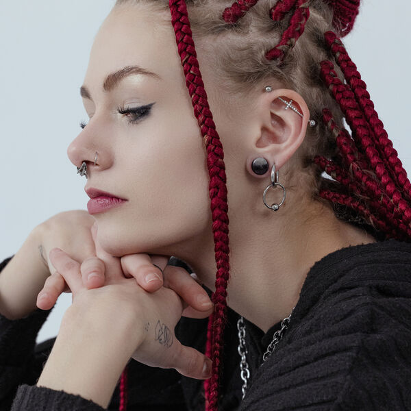 Mujer con rastas rojas lleva aros plateados y piercings en la nariz, perfil lateral