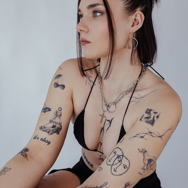 Mujer con pendientes Circular Barbell plateados y tatuajes sobre fondo claro