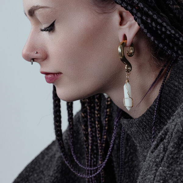 Nainen, jolla on letitetyt hiukset, käyttää kultaisia korvapainoja valkoisilla kivillä.