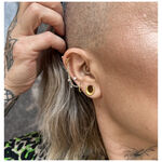 Anello piercing dorato con piccole sfere di cristallo su un orecchio con più piercing.