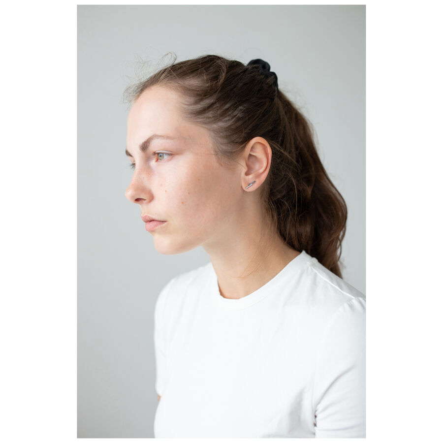 Donna con capelli castani indossa discreti orecchini d'argento su sfondo grigio