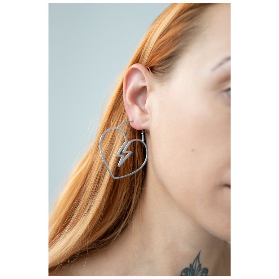 Creola a cuore in argento con design a fulmine sull'orecchio di una donna davanti a uno sfondo grigio
