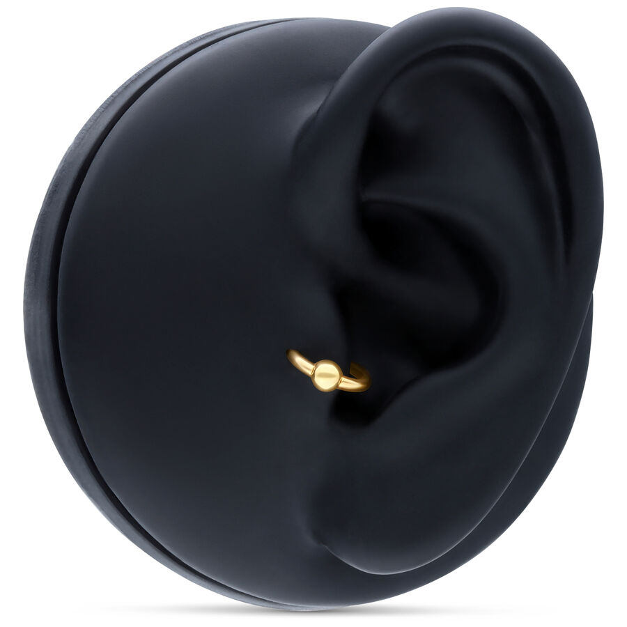 Aro de bola de presión de oro en piercing de oreja sobre fondo negro