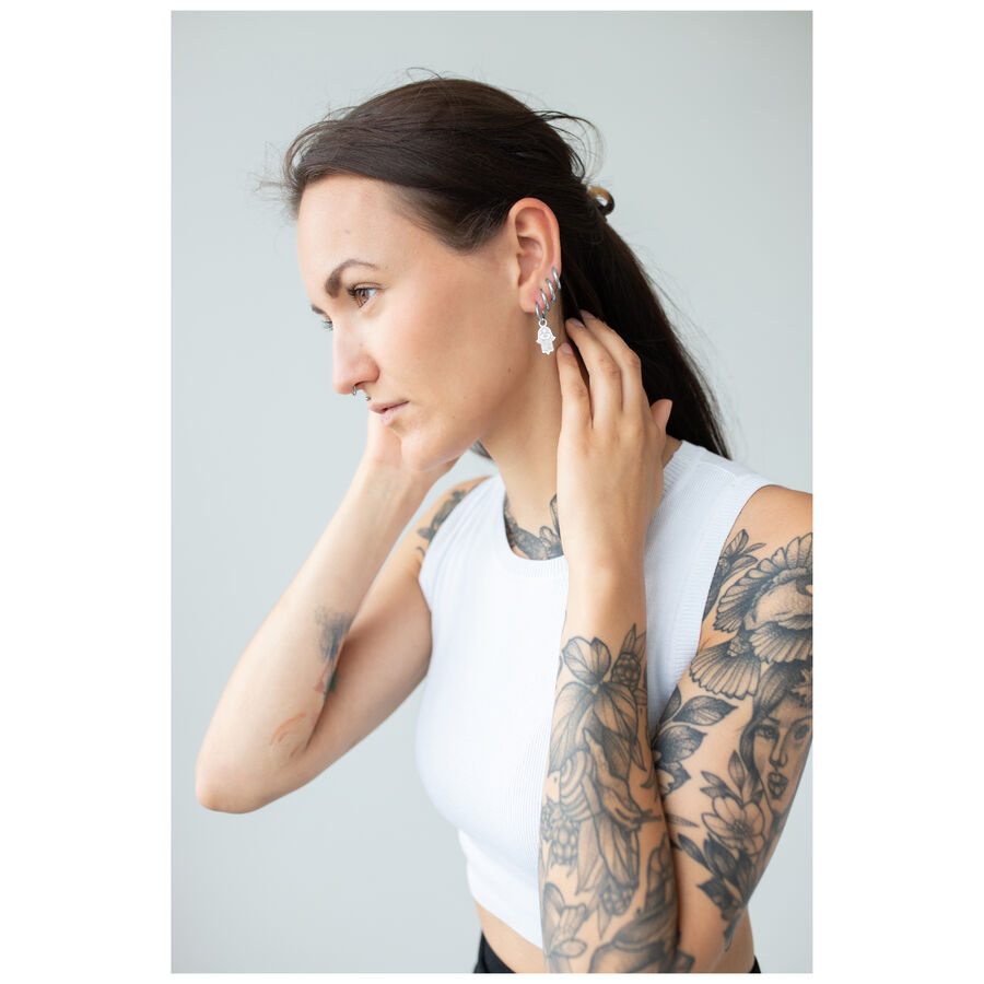 Donna con tatuaggi indossa orecchini a mano di Hamsa, top bianco, sfondo grigio