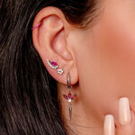 Primer plano de una oreja con varios pendientes de plata, incluyendo un pendiente colgante con cristales rojos y un colgante de pinchos.