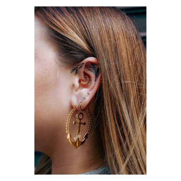 Piercings de oro con ancla y cadena, usados en la oreja de una mujer.