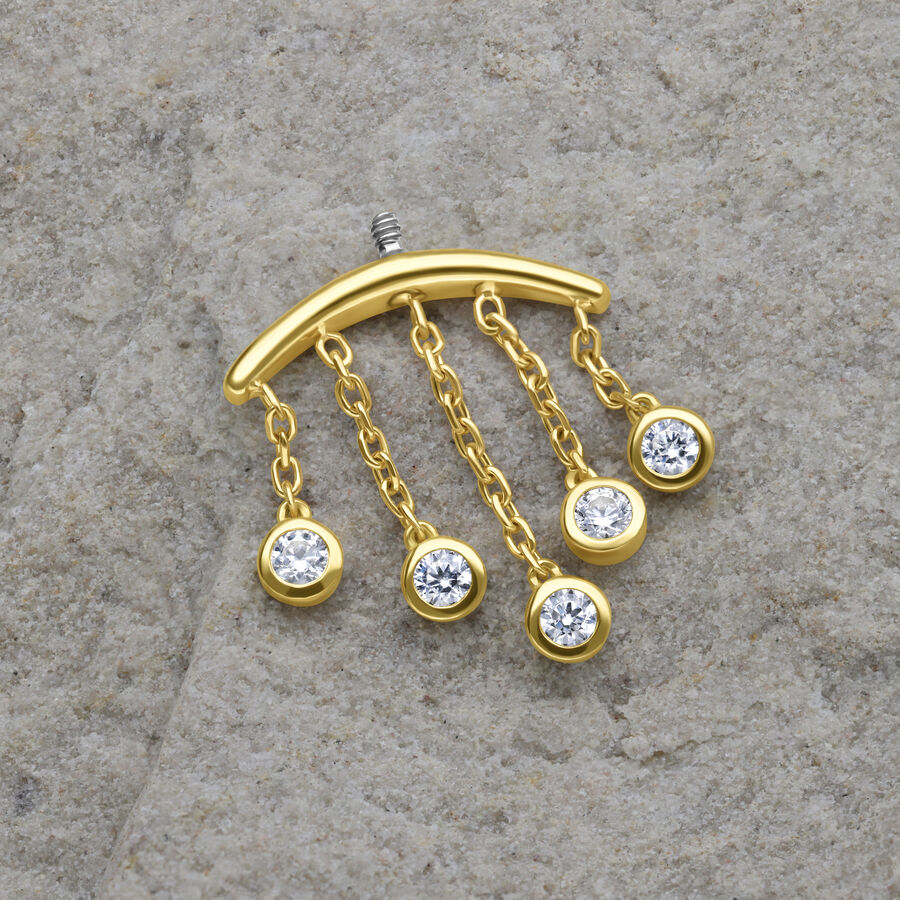 Goldener Piercing-Aufsatz mit fünf klaren Kristalltropfen auf grauem Hintergrund