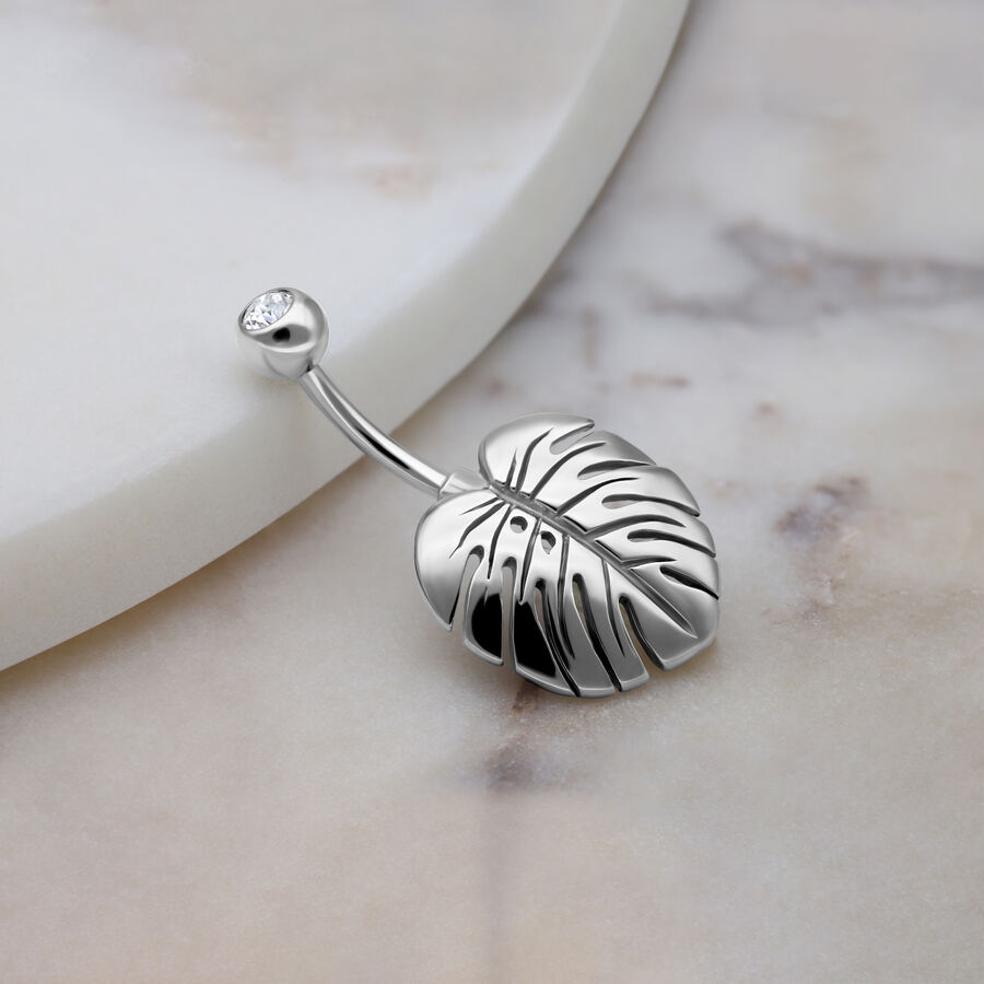 Piercing all'ombelico in argento con foglia di Monstera e cristallo su sfondo di marmo