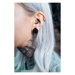 Lähikuva korvasta, jossa mustat Monstera Ear Saddles ja muita lävistyksiä, tausta epätarkka