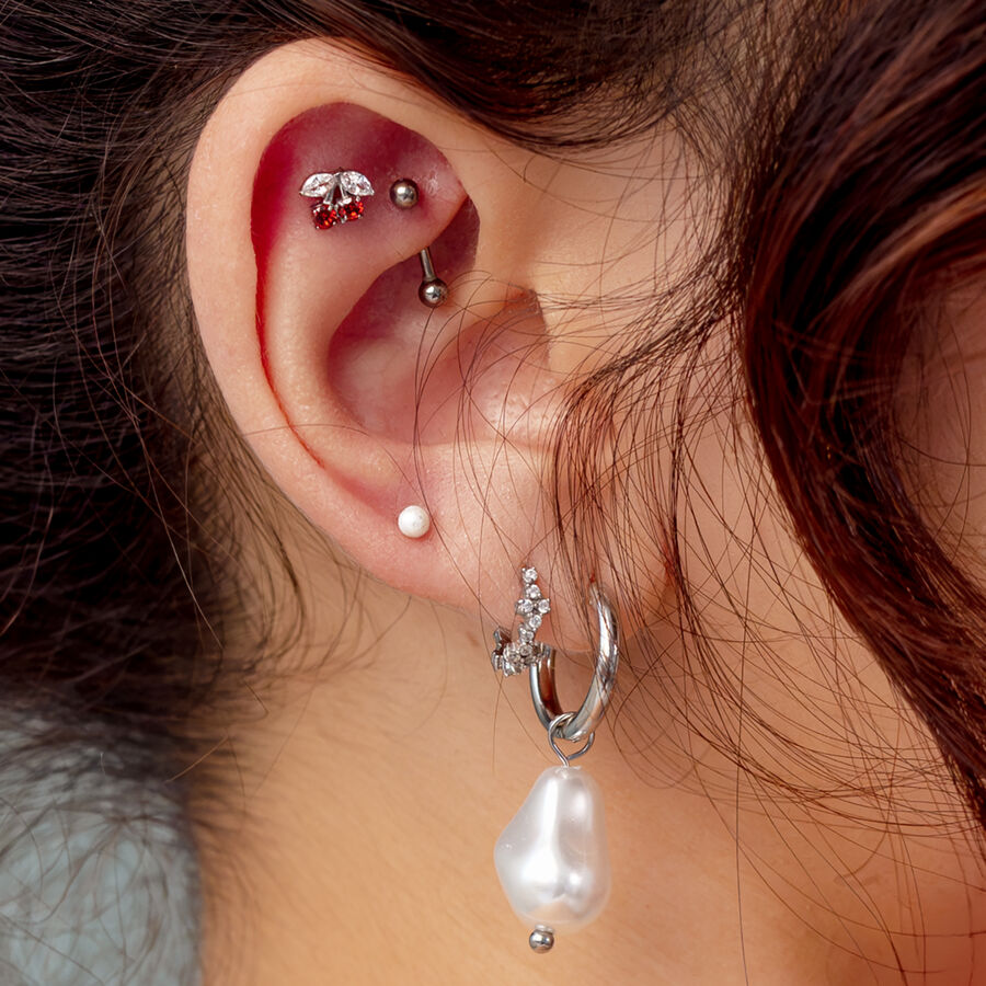 Oreja con varios piercings, incluyendo un accesorio de cereza plateado con piedra roja