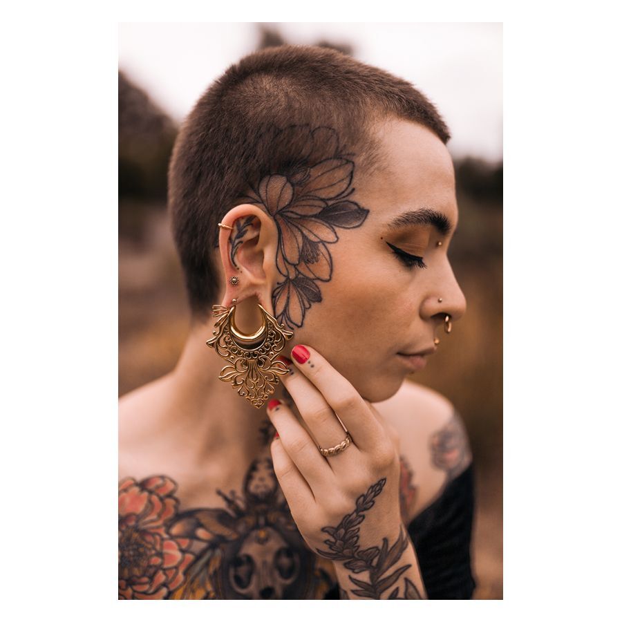 Persona con piercing Mandala Labret dorati e tatuaggi su viso e corpo