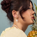 Mujer con pendientes dorados y un adorno de piña, perfil lateral