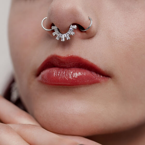 Primer plano de un clicker de septum plateado con cristales en una nariz, labios rojos visibles