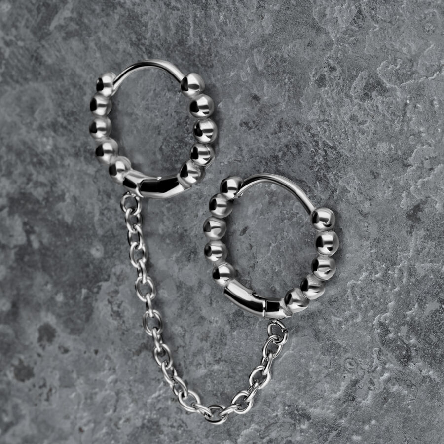 Orecchini doppio Huggie in argento con sfere e catena su sfondo grigio