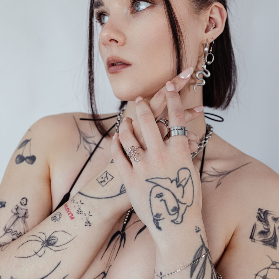 Person mit Schlangenring und Tattoos, trägt Schmuck auf weißem Hintergrund