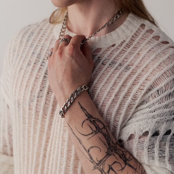 Persona con brazo tatuado lleva una pulsera Chunky plateada y un suéter tejido