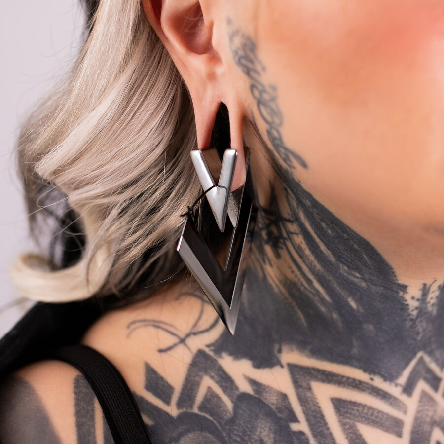 Orecchini a forma di V argento e nero in acciaio chirurgico su un orecchio con tatuaggi