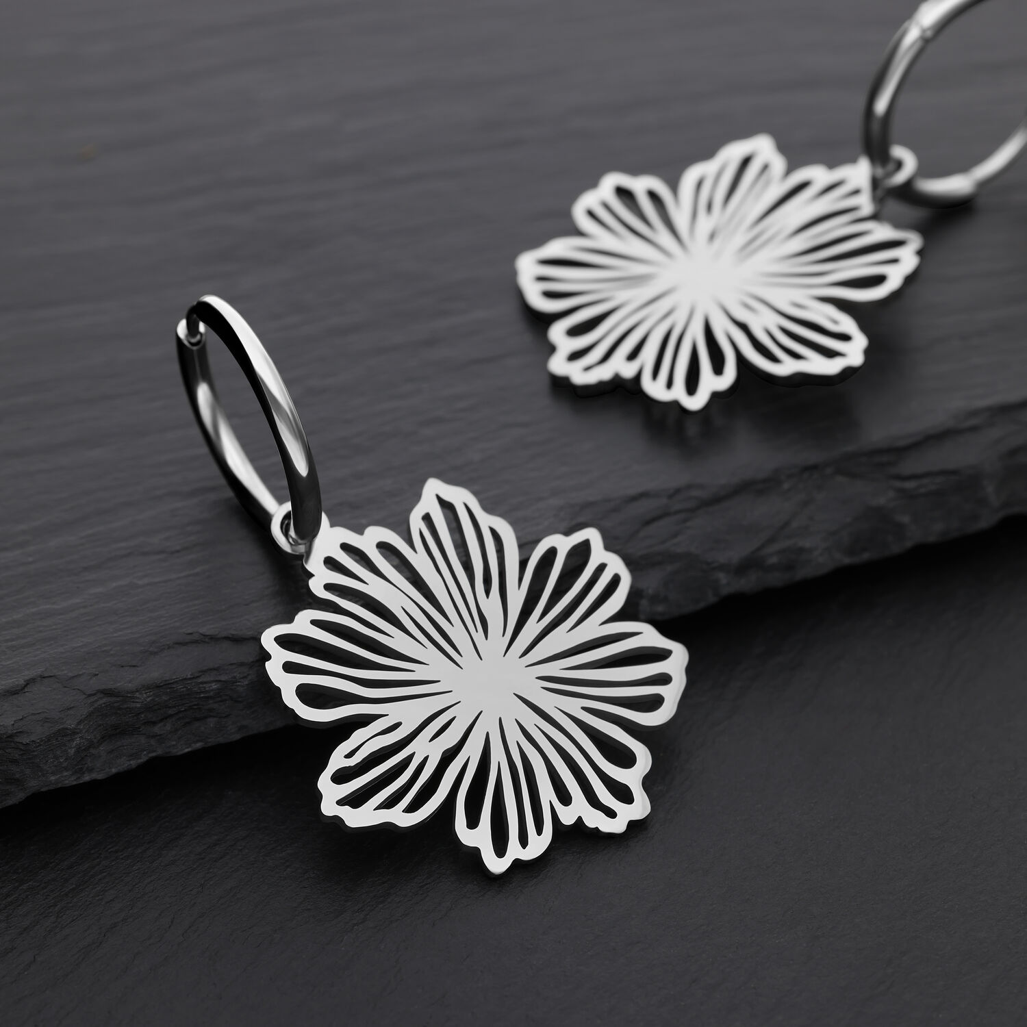 Elegante Blumen-Ohrringe aus Edelstahl Zwei silberne Ohrringe mit Blumenmuster auf schwarzem Hintergrund