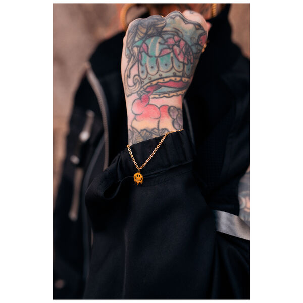 Pulsera dorada con colgante de Smiley en muñeca tatuada