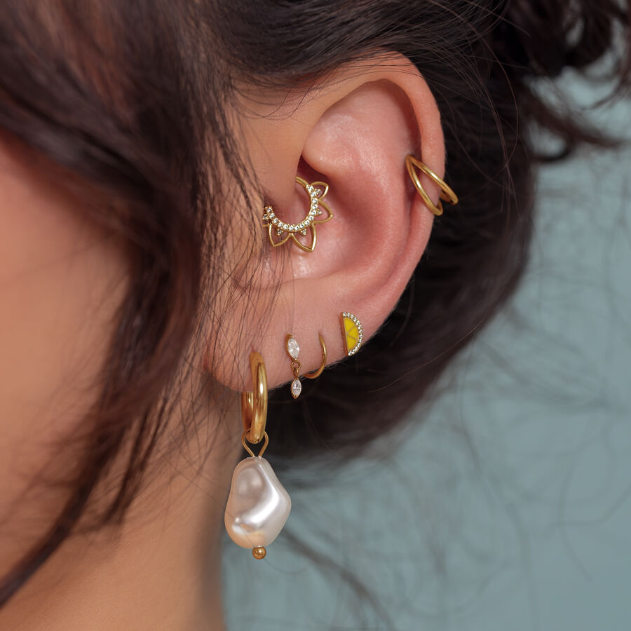 Primer plano de una oreja con varios piercings dorados, incluido un colgante de perla, sobre un fondo azul claro
