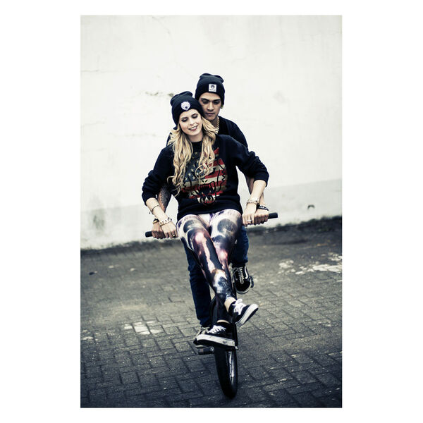 Joven mujer y hombre en bicicleta, llevan sudadera Wildcat® negra con diseño USA