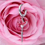 Pendiente de plata con cristales rojos, en forma de flor, frente a una rosa rosa