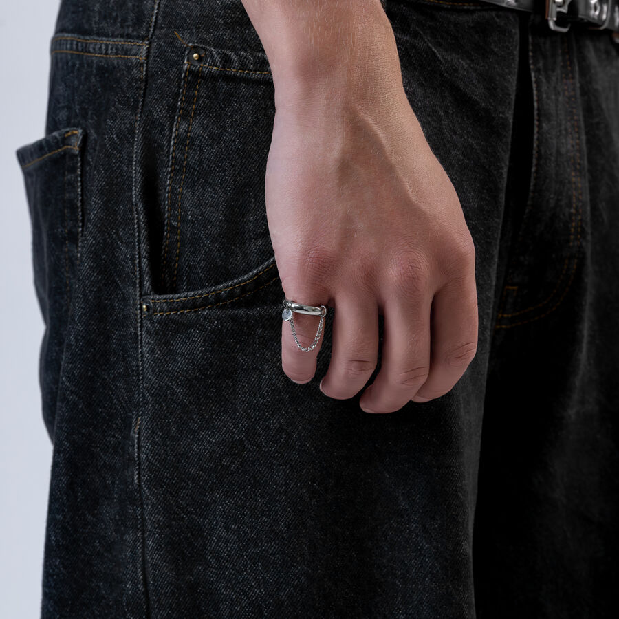 Mano con anello a catena argento, indossato su jeans scuri, primo piano
