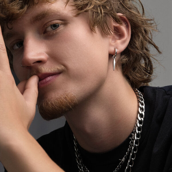Joven con cabello rizado lleva pendientes de plata y cadenas, fondo gris