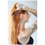 Mujer con cabello rojo lleva Sphynx Hoops plateados sobre fondo claro