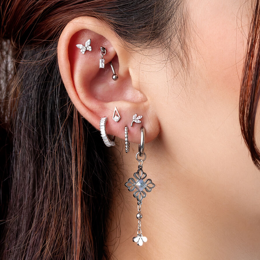 Ohr mit mehreren silbernen Piercings, darunter ein hängendes Blumenmotiv, auf hellbraunem Hintergrund