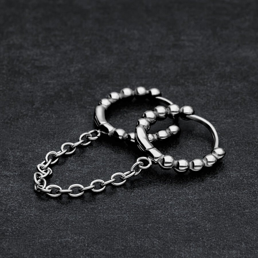 Due anelli piercing Huggie neri collegati con sfere su sfondo scuro