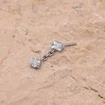 Attacco per piercing in titanio argento con due cristalli chiari su sfondo color sabbia