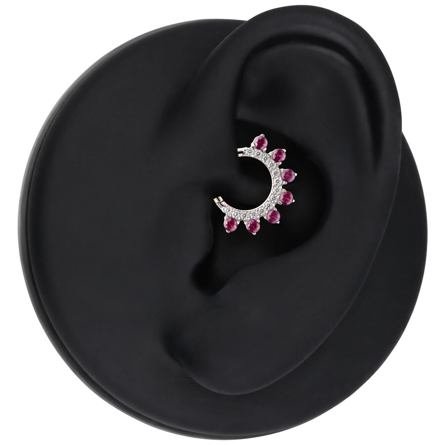 Anillo de piercing plateado con cristales rojos en un expositor de oreja negro