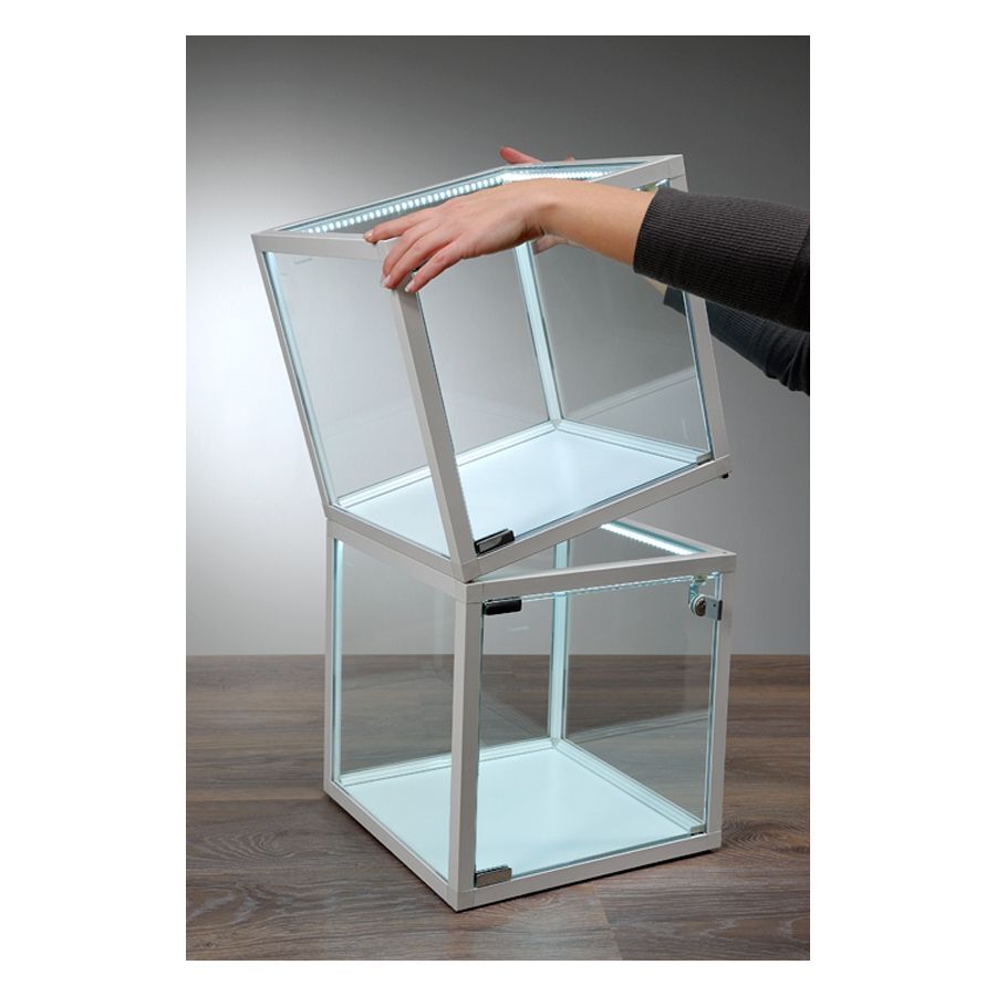 Due cubi vetrina di vetro bianchi con strisce LED su tavolo di legno, una mano solleva il cubo superiore