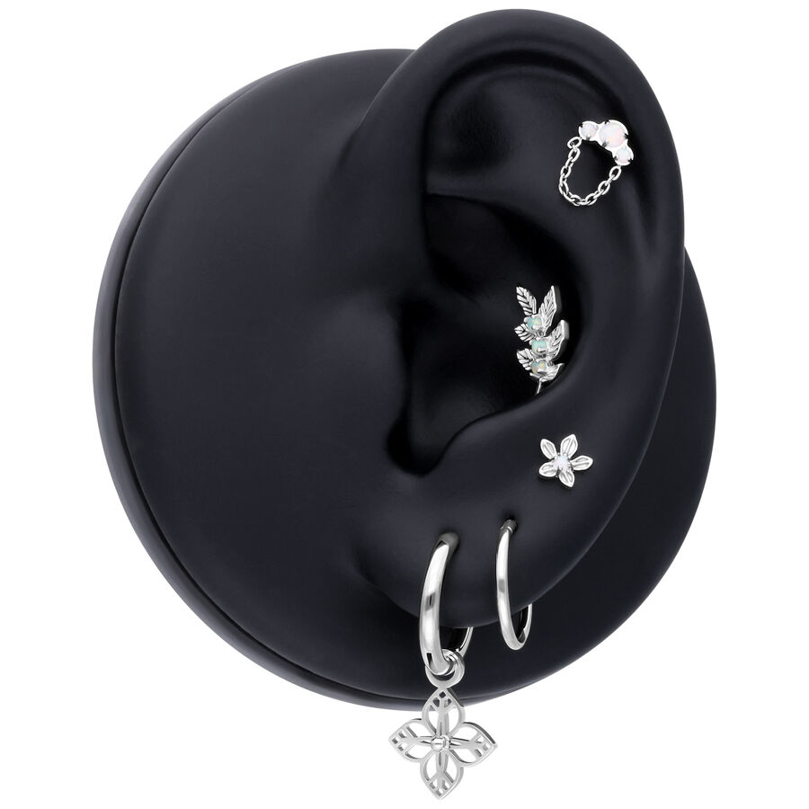 Soporte de modelo de oreja negro con varias joyas, incluyendo un Hinged Ring de oro blanco con colgante de flor.