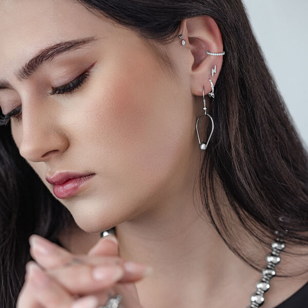 Mujer con pendientes de anillo en forma de lágrima plateados frente a un fondo gris