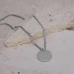 Collana d'argento con ciondolo rotondo su pavimento in pietra chiara