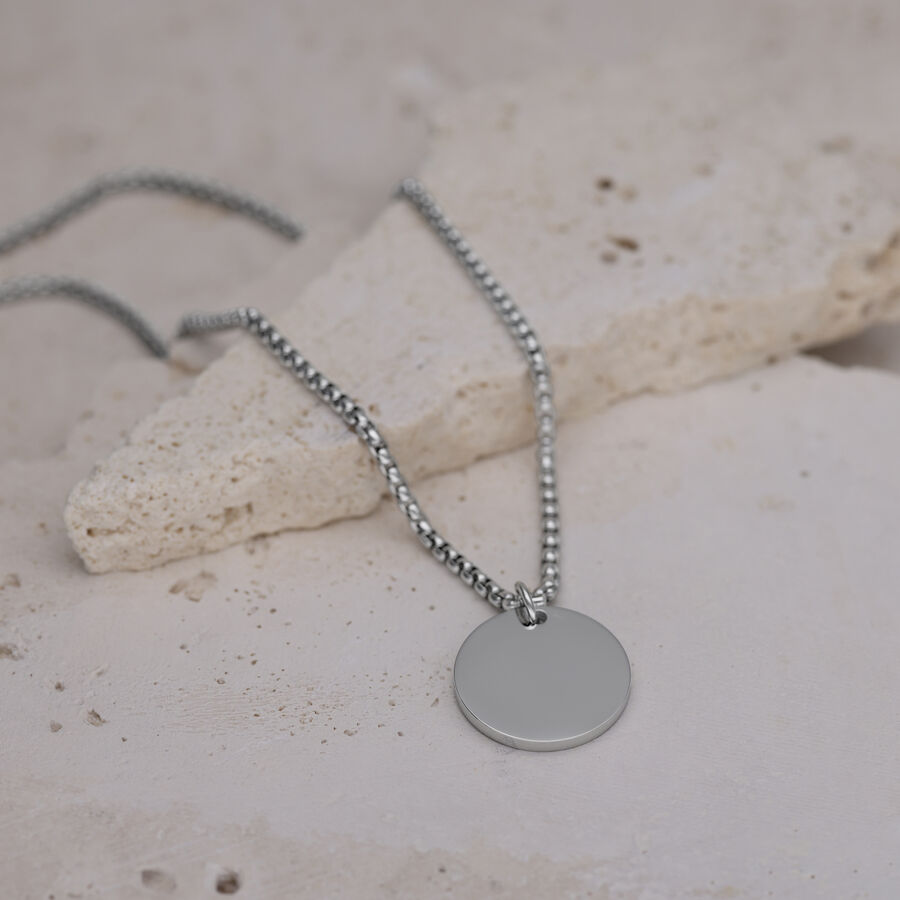 Collana d'argento con ciondolo rotondo su pavimento in pietra chiara