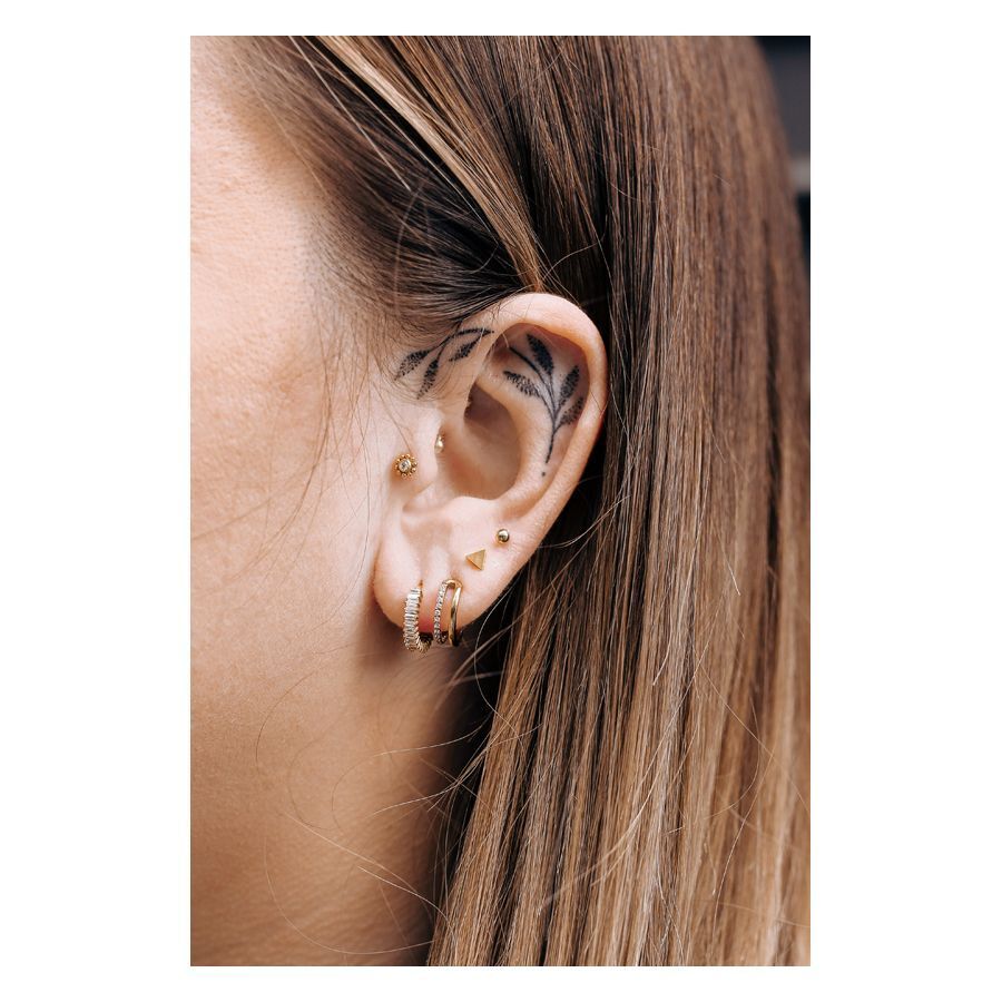 Piercing Triangle Barbell in oro all'orecchio di una persona con altri piercing e tatuaggio sull'orecchio