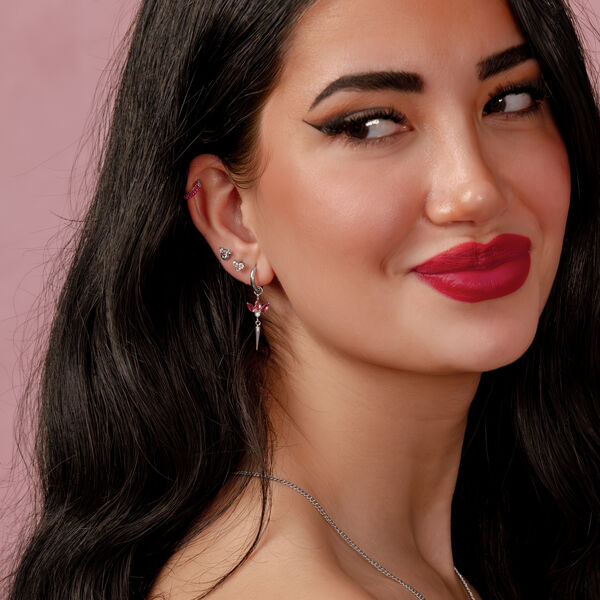 Mujer con cabello negro largo y pendiente de plata con rubí rojo sobre fondo rosa